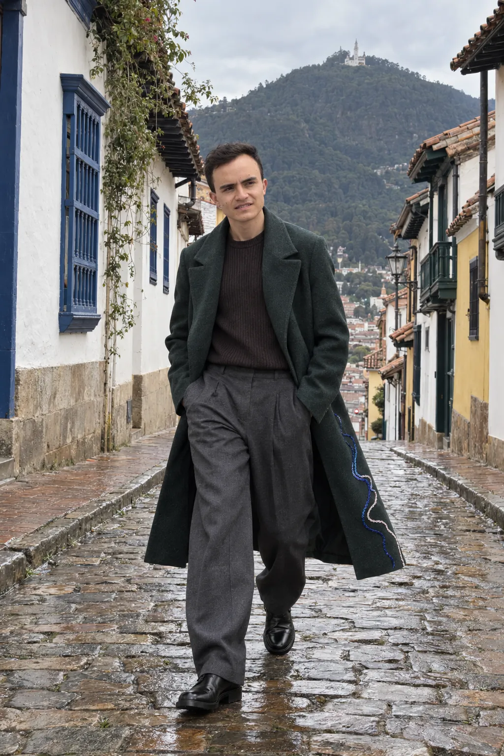 Days camina por una calle empedrada de La Candelaria, en Bogotá, con el abrigo largo verde bosque. Toma de campaña.