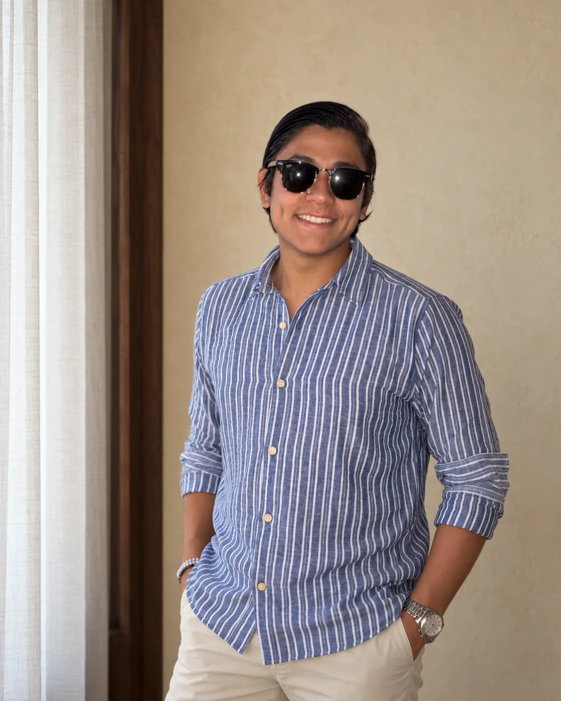 Sebastián Bueno con camisa de rayas azules y blancas y gafas oscuras, junto a una ventana.